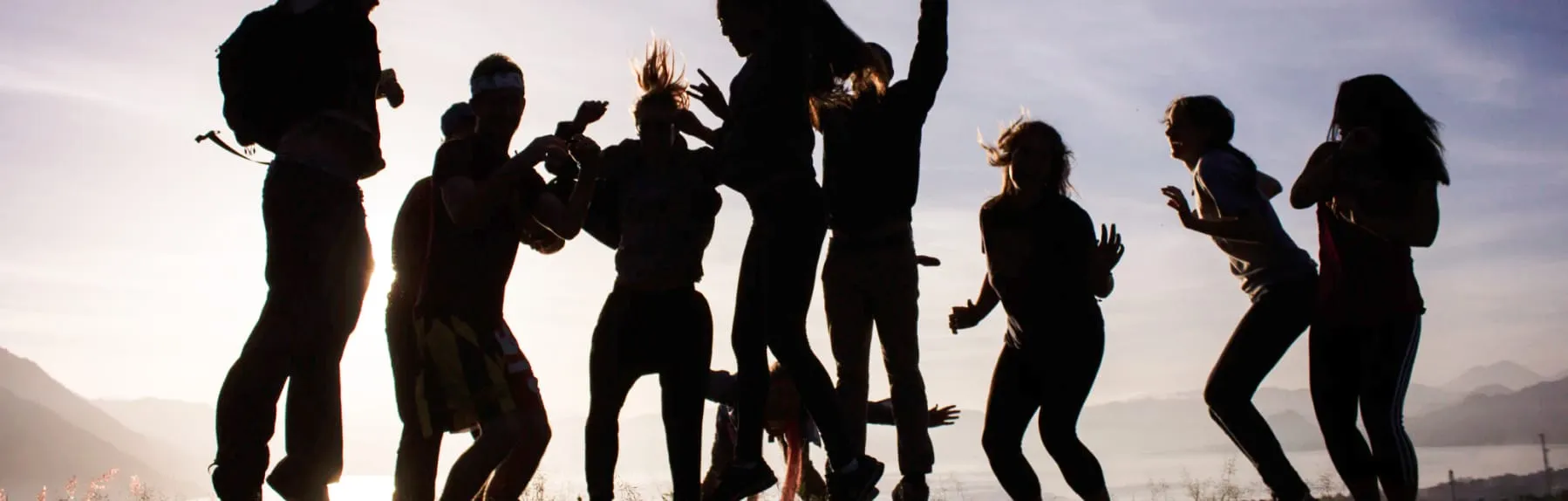 Group of young people jumping around on a cliff overlooking the ocean.