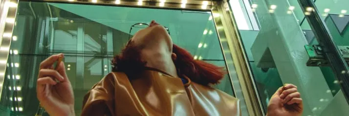 Girl wearing glasses looking upward inside of an elevator.